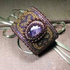 a purple and gold beaded ring on top of a box