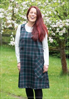 a woman with red hair wearing a green and black plaid dress standing in front of a tree