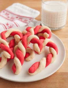 some red and white cookies are on a plate next to a glass of milk,