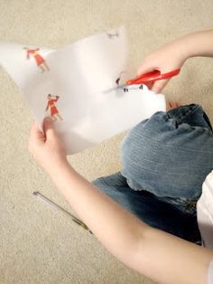 a woman sitting on the floor cutting paper with scissors