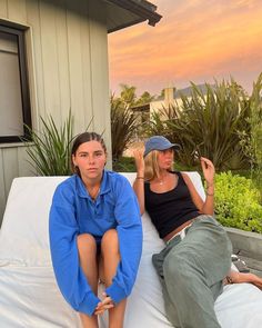 two women sitting on a white couch in front of a house