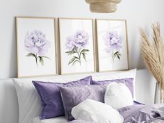 a bed with purple and white flowers on the wall above it, along with two framed pictures