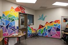 an office decorated with colorful triangles and birds painted on the wall, along with two desks