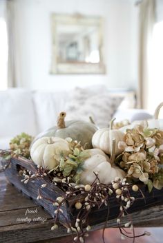 a wooden tray filled with white pumpkins and flowers on top of a table in a living room