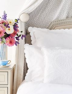 a vase with flowers in it sitting on top of a bed next to two pillows