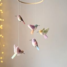 several small birds hanging from a string in a room with lights on the wall behind them