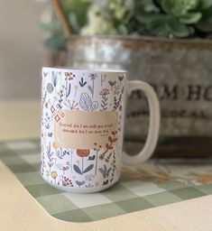 a white coffee mug sitting on top of a table next to a potted plant