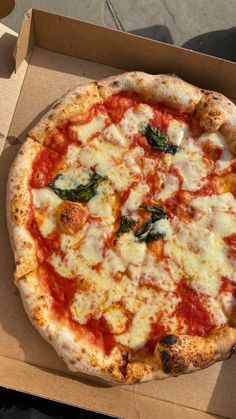 a pizza with cheese and spinach on it sitting in a cardboard box next to a person's hand