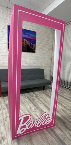 a pink frame sitting on top of a hard wood floor next to a gray couch