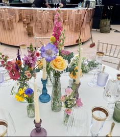 a table topped with lots of vases filled with different types of flowers and candles