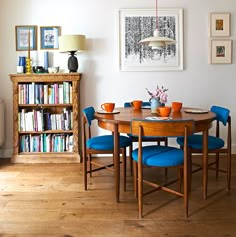 a dining room table with blue chairs and bookshelf in the backround