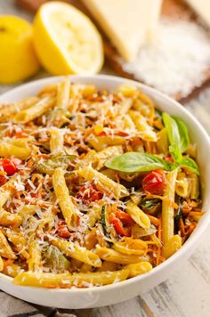 a white bowl filled with pasta and vegetables on top of a table next to sliced lemons