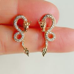 a pair of gold and diamond earrings on a person's finger in front of a white background