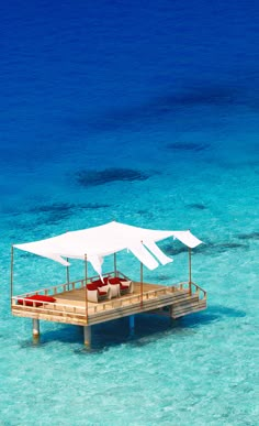 a dock with chairs and umbrellas in the water near some blue water, while one boat is floating on it's side