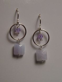 pair of earrings with purple stones and silver hoops on white table top next to wall