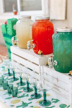 there are many different colored drinks in mason jars on the table with cups and glasses