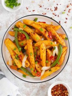 a white bowl filled with french fries covered in sauce and green peppers next to two small bowls of seasoning