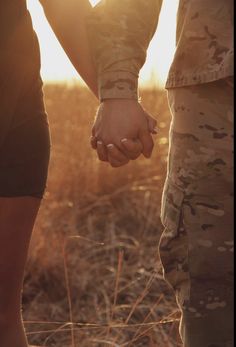 two people holding hands while standing in a field with the sun shining down on them