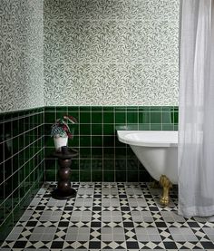 a bath tub sitting next to a white toilet in a green and black tiled bathroom