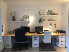 a home office with two desks and white drawers on the wall, along with a clock