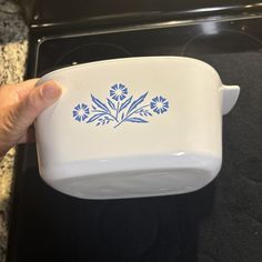 a hand is holding a blue and white ceramic bowl with flowers on it in front of an oven