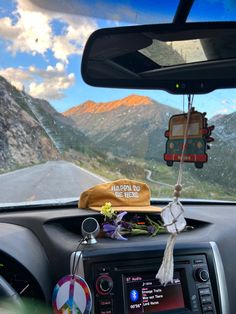 the dashboard of a car with a hat hanging from it's dash board and mountains in the background