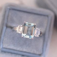 an emerald cut ring with three baguettes sits on top of a velvet box