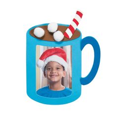 a blue coffee mug with a red and white striped hat on it, next to a photo of a young boy wearing a santa's hat