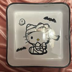 a hello kitty glass plate with bats and skulls on the side, sitting on a bed