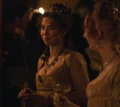 two women dressed in period clothing standing next to each other with wine glasses on their laps