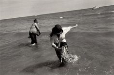 black and white photograph of two people in the ocean with one person reaching for something