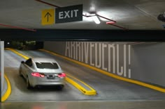 a car driving under an exit sign in a parking garage with yellow lines on the floor