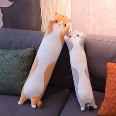 two stuffed cats sitting on the back of a couch next to each other in front of pillows