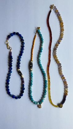 three beaded necklaces are lined up on a white surface, one is blue and the other is yellow