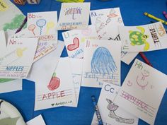 many children's handwritten and colored papers on a blue table with crayons