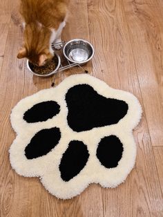 a cat eating food out of a bowl on the floor next to it's paw print rug