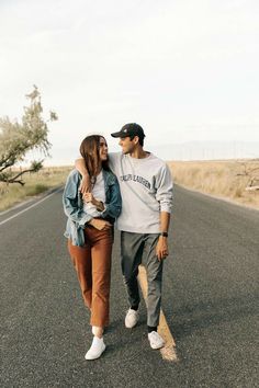 a man and woman walking down the middle of an empty road with their arms around each other