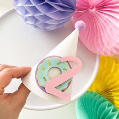 a hand holding a paper cone with a doughnut on it and some tissue pom - poms