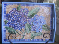 a blue and yellow mosaic tile with flowers on it's side is displayed in front of a window