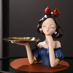 a figurine sitting on top of a table with a plate in front of her