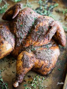 roasted chicken on a baking sheet with herbs and seasoning sprinkled around it