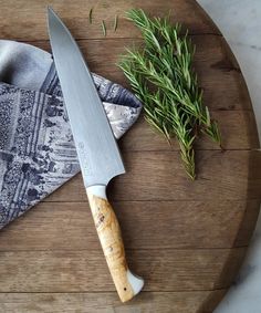 a knife sitting on top of a wooden cutting board next to a napkin and sprig of rosemary