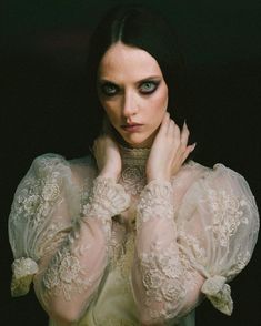 a woman with black hair and blue eyes is wearing white lace gloves while holding her hands to her face