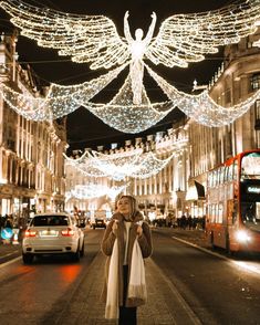 a woman standing in the middle of a street with christmas lights strung all around her