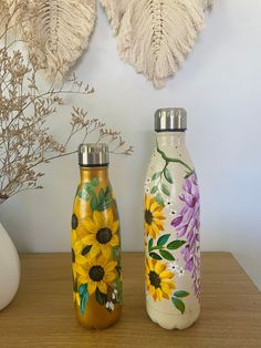 two vases with flowers painted on them sitting on a table next to a plant