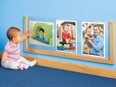 a baby sitting on the floor in front of three pictures hanging on a wall with a wooden frame