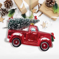 an old red truck with a christmas tree on the back is surrounded by presents and pine cones