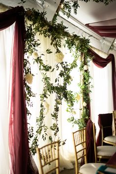 chairs are lined up in front of a window with flowers hanging from the ceiling and drapes over them