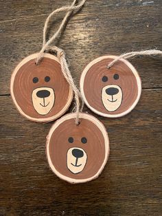 three wooden ornaments with bear faces on them hanging from twine string and wood planks