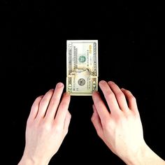 two hands reaching for a one dollar bill on a black background with space for text